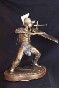 Dynamic bronze sculpture of the Murmillo type of gladiator carrying shield, sword and wearing a heavy helmet. Fighting stance with ax embedded into the shield.