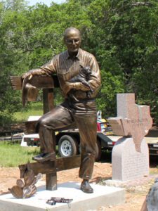 Outdoor bronze rancher statue beside memorial stone