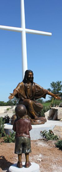 Tall white cross behind bronze Jesus